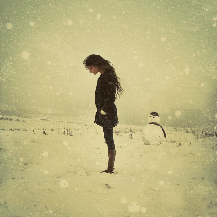 Woman standing in snow next to a snowman