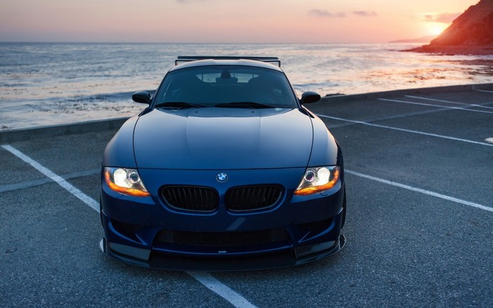 Blue BMW Z4 sports car parked by the ocean at sunset