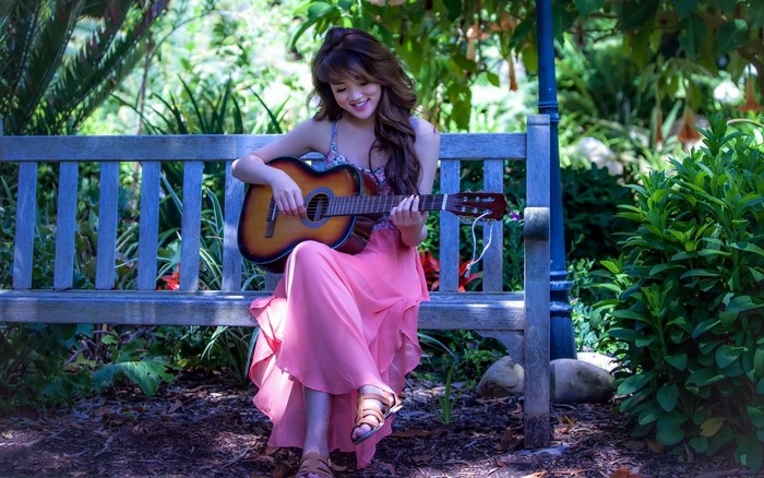 Woman playing guitar on a bench in a garden