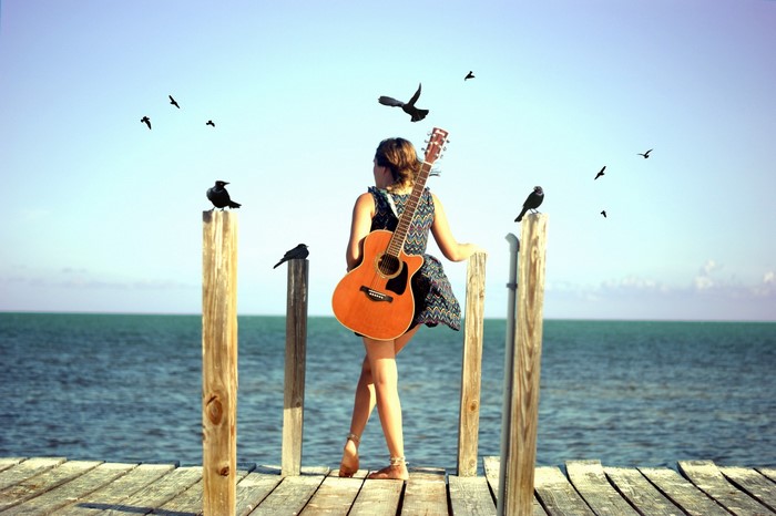 Woman with guitar on a pier with birds