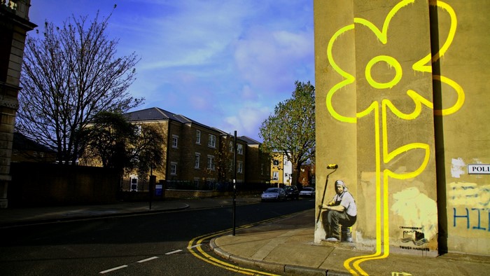 Graffiti artist painting a flower on a building wall