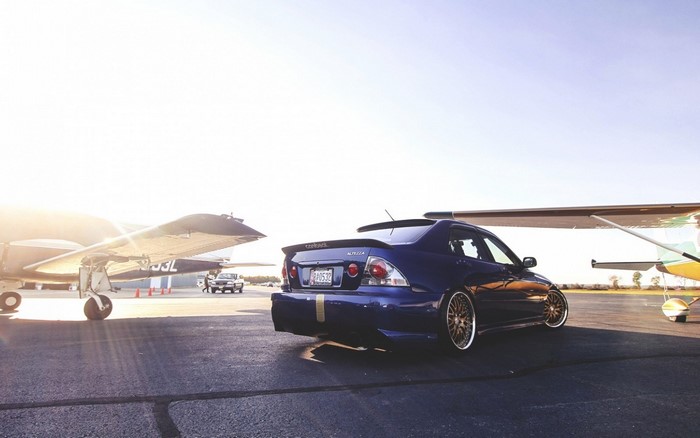 Blue Lexus IS Altezza parked by airplanes on tarmac