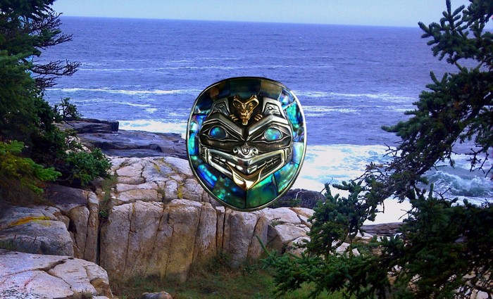 Haida mask with abalone inlay against a rocky coastline and ocean