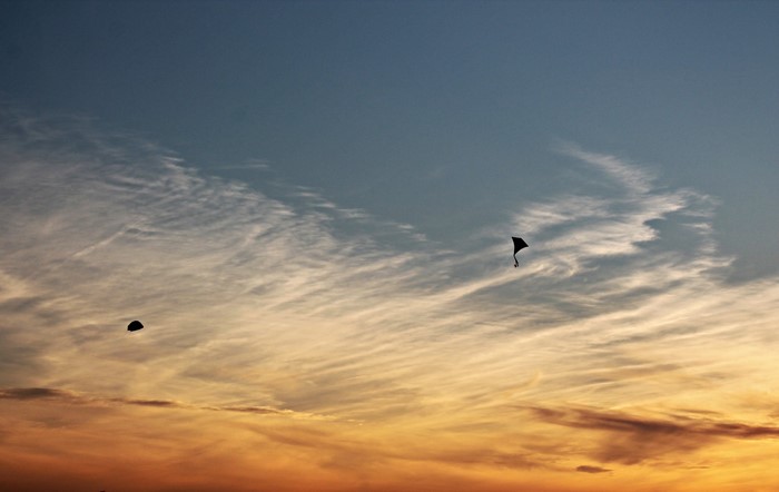 Two kites flying in the sky at sunset