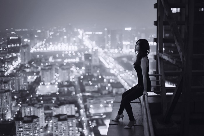 Woman sitting on edge of skyscraper overlooking city at night
