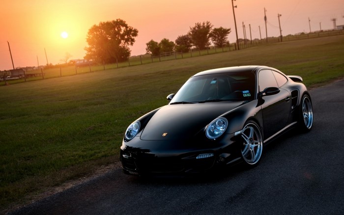 Black Porsche 911 Turbo S parked on a road at sunset