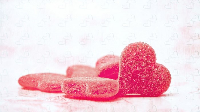Red heart-shaped candies on a pink heart patterned background