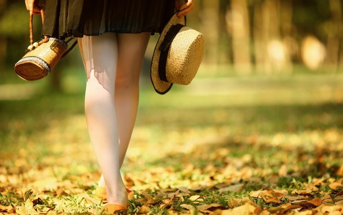 Woman holding a straw hat and a bag, walking in autumn park