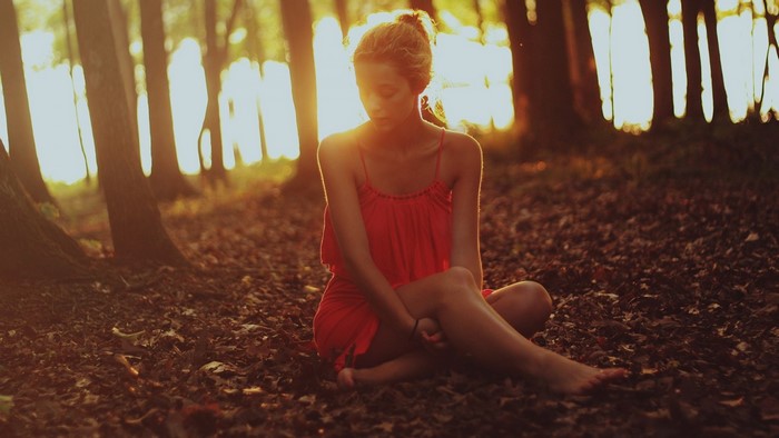 Woman in red dress sitting in a forest at sunset