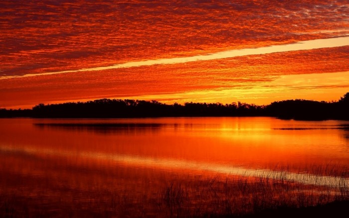 Sunset over a lake with orange clouds and reflection