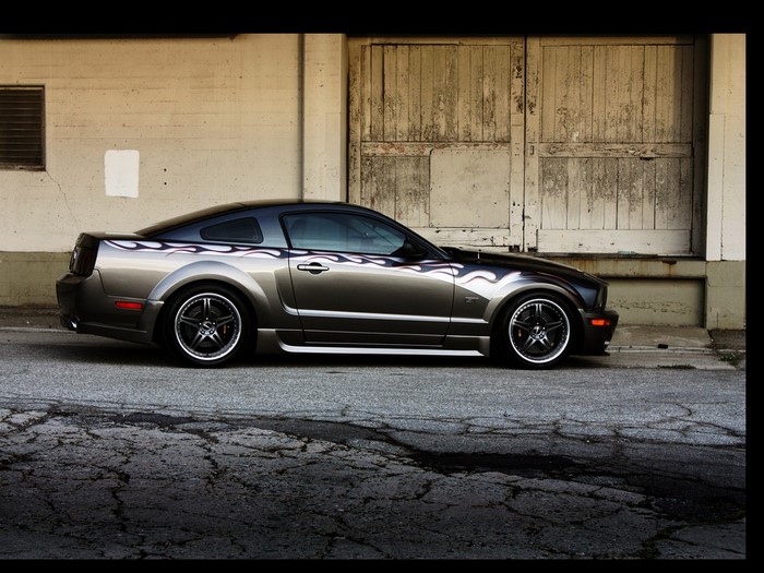 Gray Ford Mustang with flame decals parked by a building