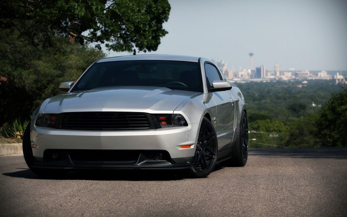 Silver Ford Mustang parked on a hill overlooking a city