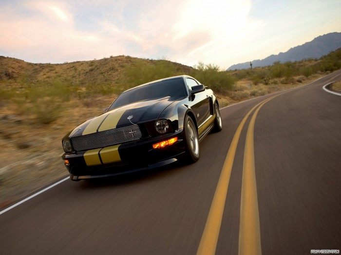 Black Ford Mustang with yellow stripes on a road
