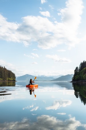 Woman kayaking on a calm lake with mountains in the background