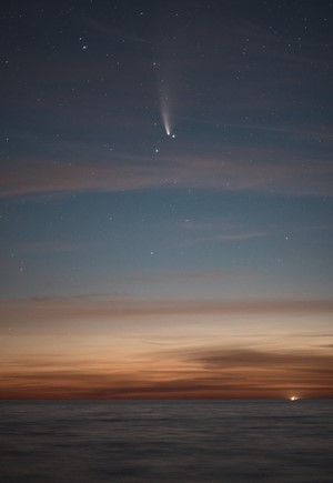 Comet and stars over the ocean at dusk
