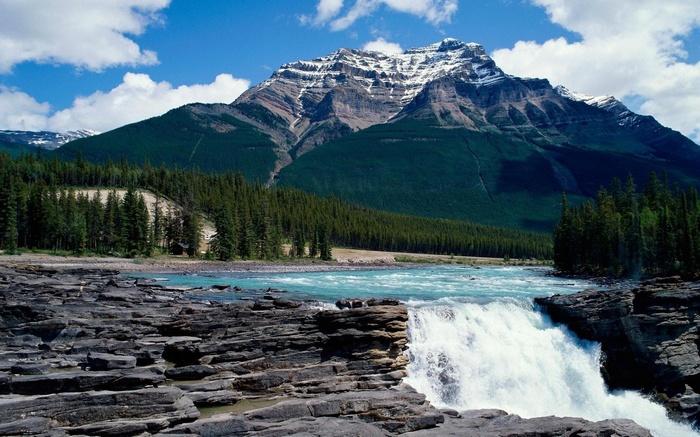 Waterfall flowing over rocks with a mountain and forest background