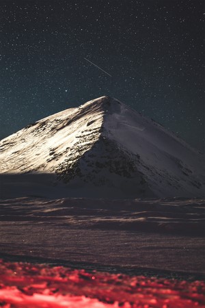 Snowy mountain peak under a starry night sky with a shooting star