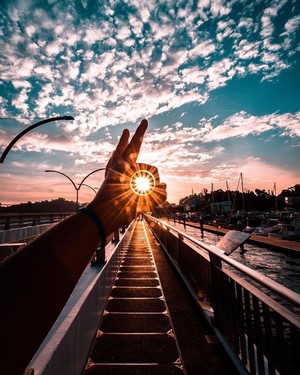 Person holding sun over bridge at sunset