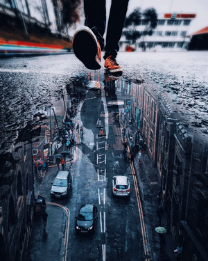 Man's feet stepping into a puddle reflecting a city street