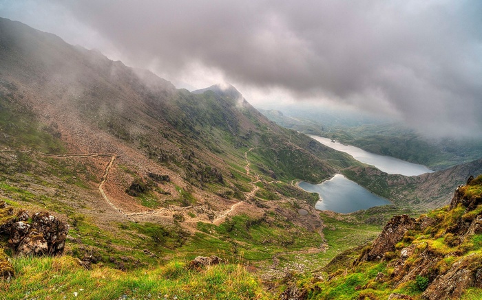 Mountain path overlooking lakes under cloudy sky