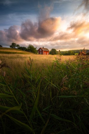 Red house in a field at sunset with dramatic clouds