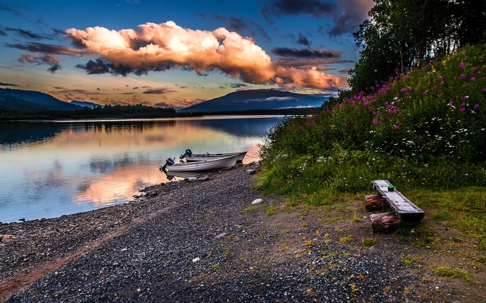 Boats on a lake shore with mountains and sunset clouds
