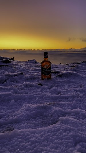Ballantine's whisky bottle in snow at sunset