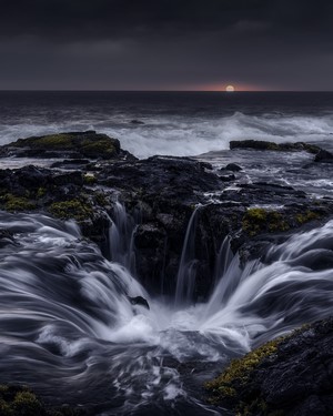 Sea cave waterfall at dusk with sunset over the ocean
