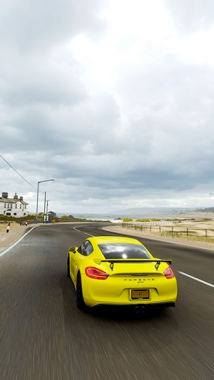 Yellow Porsche Cayman GTS driving on a coastal road in Forza Horizon 4