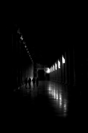 Silhouettes of people in a dark, colonnaded hallway
