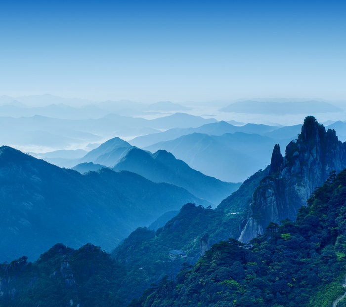 Layered blue mountains shrouded in fog under a clear sky