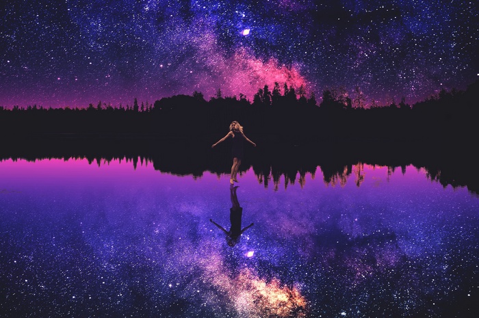 Woman standing in lake under starry sky reflection