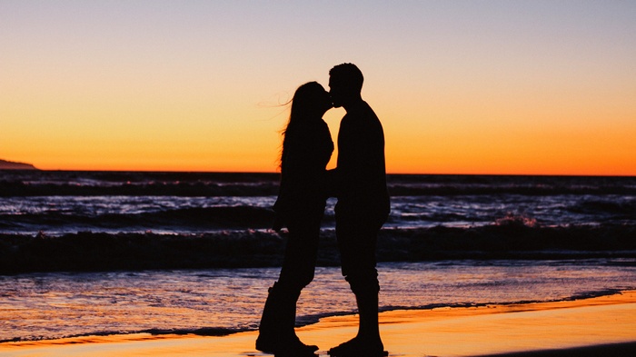 Couple kissing on beach at sunset silhouette