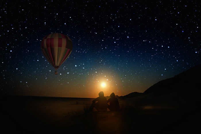 Couple watching hot air balloon under starry sky at sunset