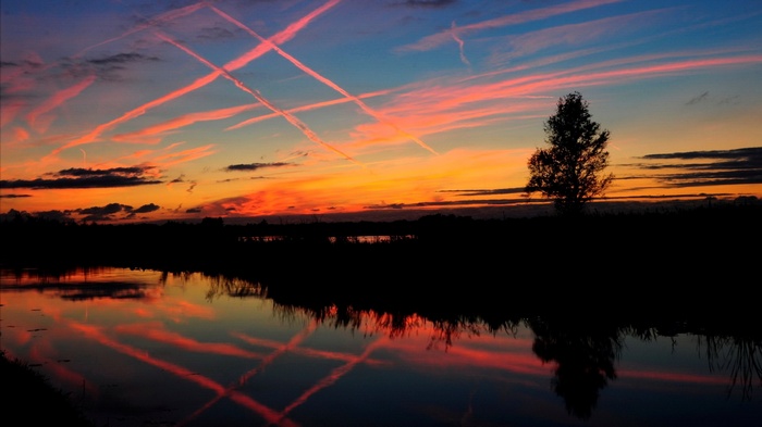 Sunset sky with contrails reflected in water