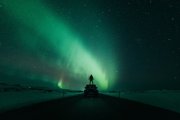 Man on Jeep watching Aurora Borealis in Iceland