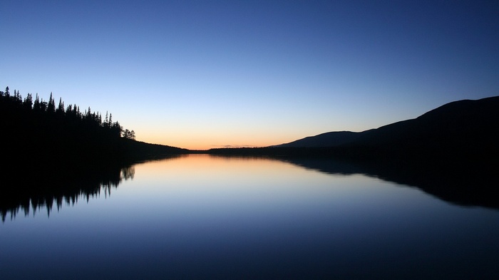 Lake reflecting trees and mountains at dusk