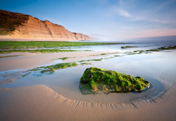Coastal beach with mossy rocks and cliffs at sunrise 4K