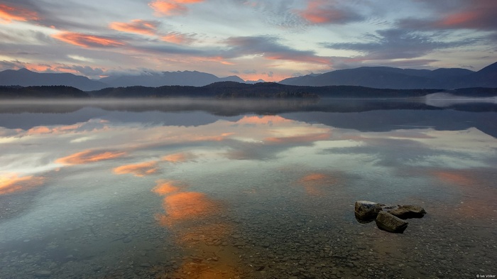Calm lake reflecting colorful clouds and mountains at sunrise