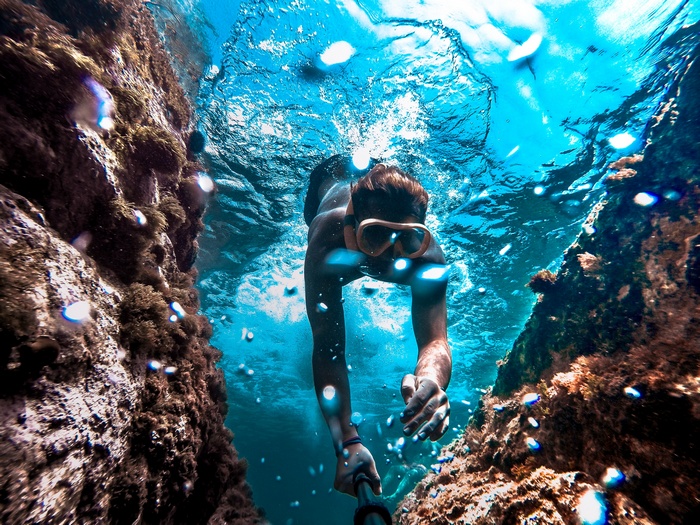 Man snorkeling between rocks in clear blue water 4K