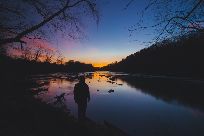 Man silhouetted by a river at sunset