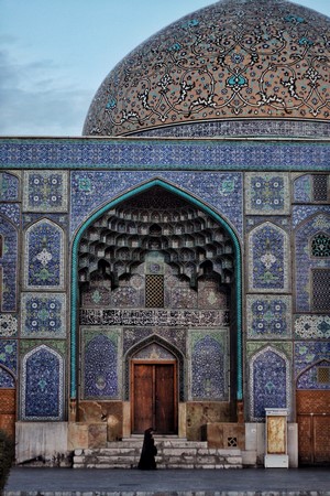 Woman in black walks up steps to ornate mosque entrance