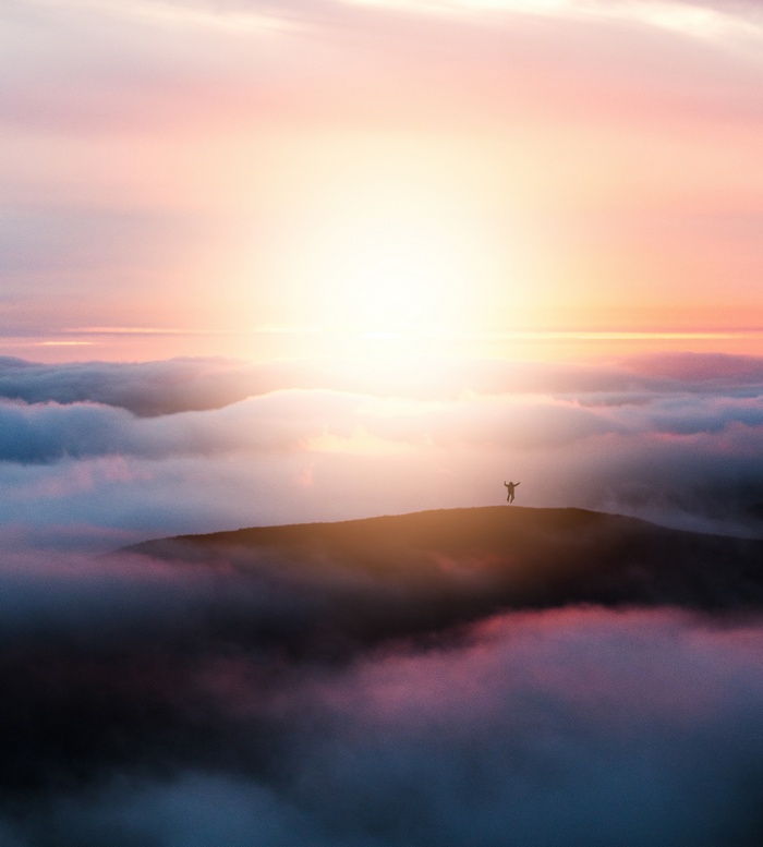 Person on mountain peak above clouds at sunrise