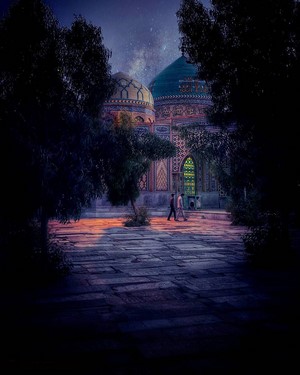 Two people walk past a mosque in Iran at night