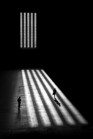 Two people walk through a room with striped shadows.