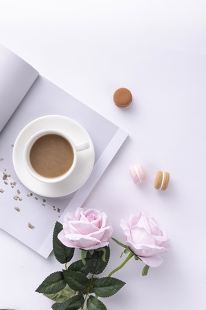 Coffee cup with macarons and pink roses on a book