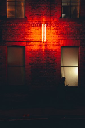 Silhouette in window with red neon light on brick building at night