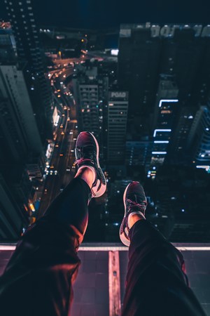 Person sitting on edge of building overlooking city at night