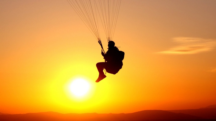 Paraglider silhouetted against a vibrant sunset