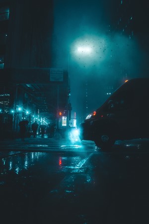 Dark rainy city street at night with car